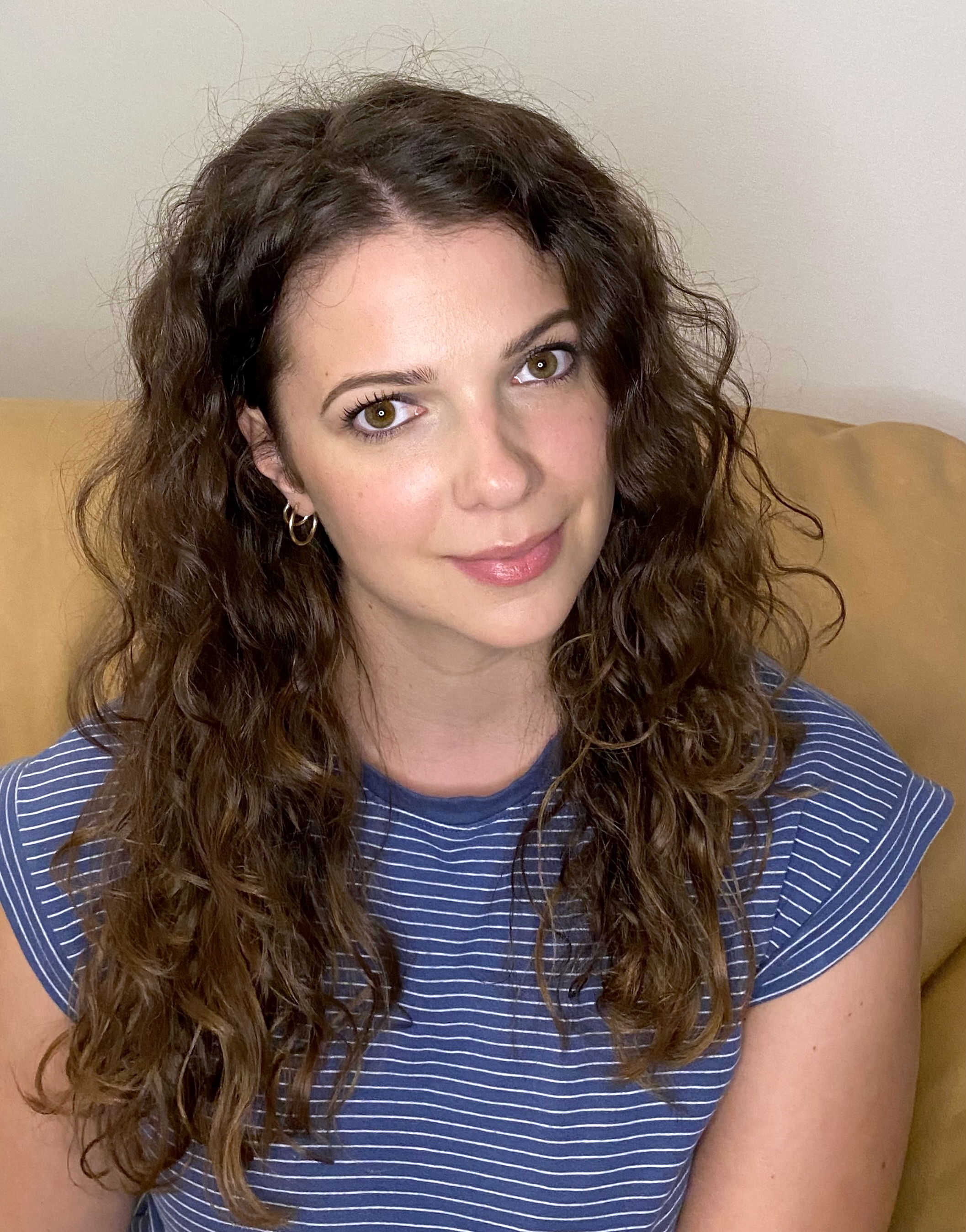 A young woman with longer curly hair smiles for the camera.